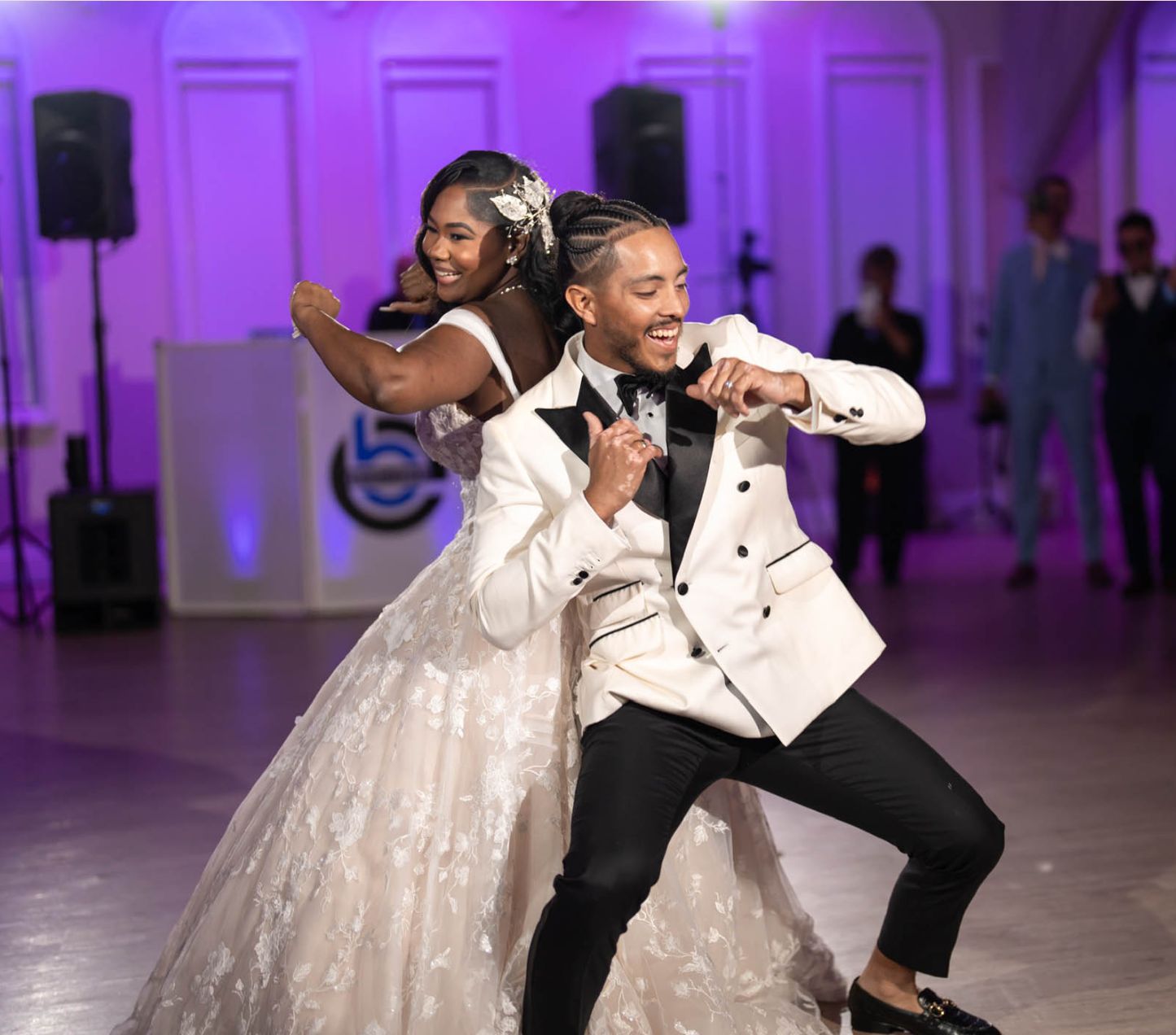 A bride and groom in formal attire dance enthusiastically together at their wedding reception in a decorated indoor venue.